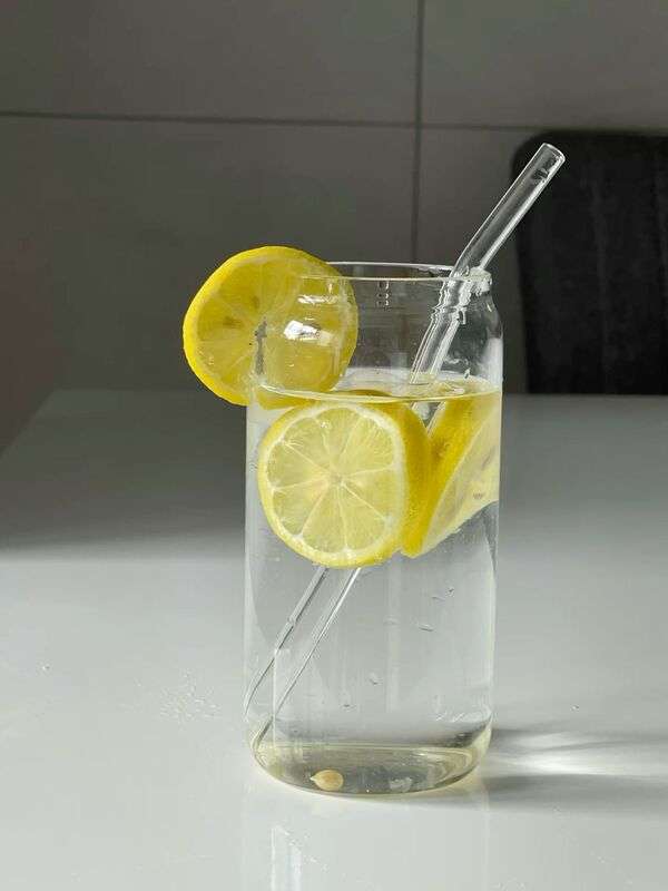 Vaso de agua fría con hielo y rodajas de limón sobre una mesa clara